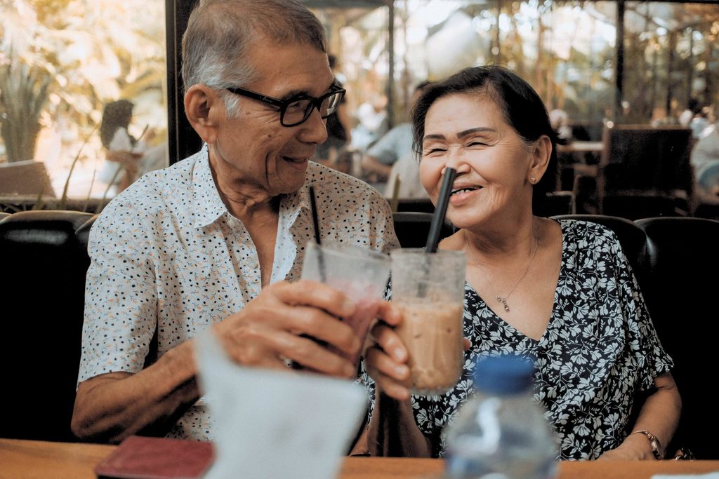 Happy senior couple sharing a moment with iced beverages in a cozy cafe setting.